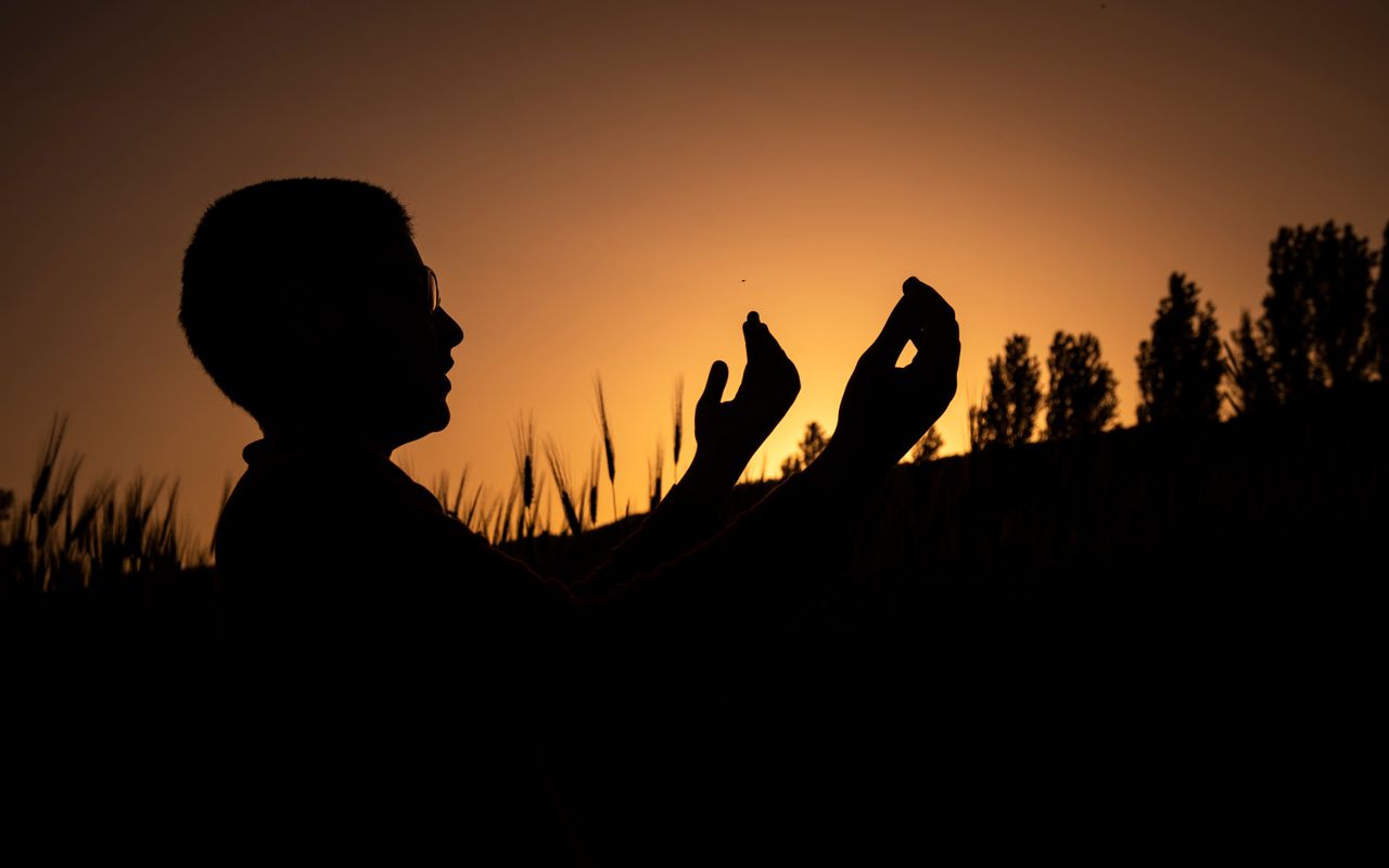 Silhouette of a man with outstretched hands in a field during sunset in Çameli, Türkiye.