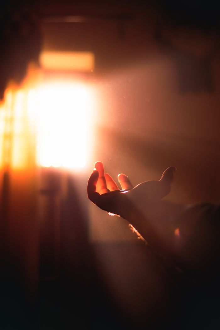 A silhouetted hand reaching out to a bright light with dramatic shadows.