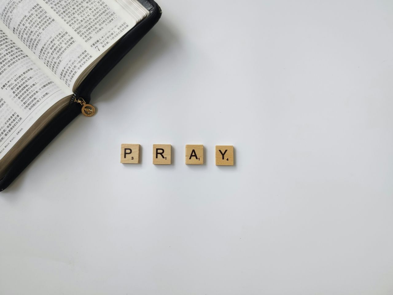 Flat lay of an open Bible and letter tiles spelling 'Pray' on a white background, symbolizing religious reflection.
