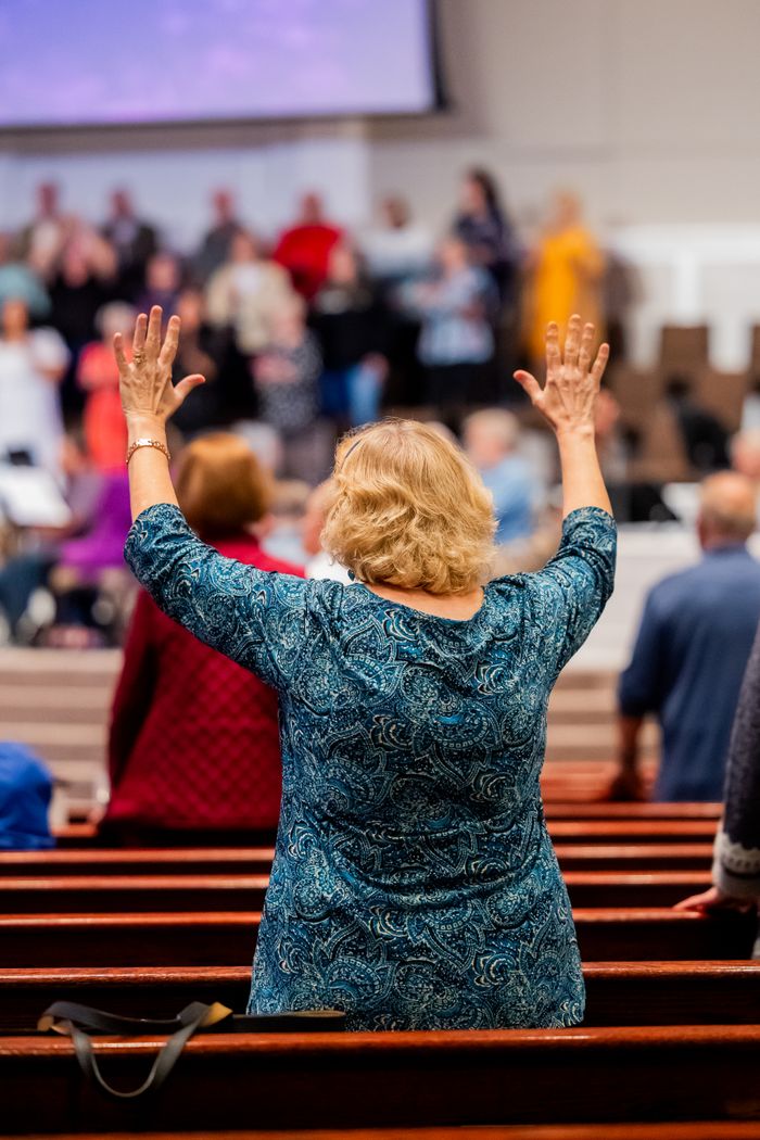 A woman raising her hands in worship during a church service with a choir in the background.